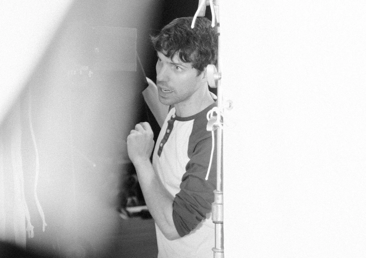 Black and white photo of Graham Nolte directing on set, leaning against a wall