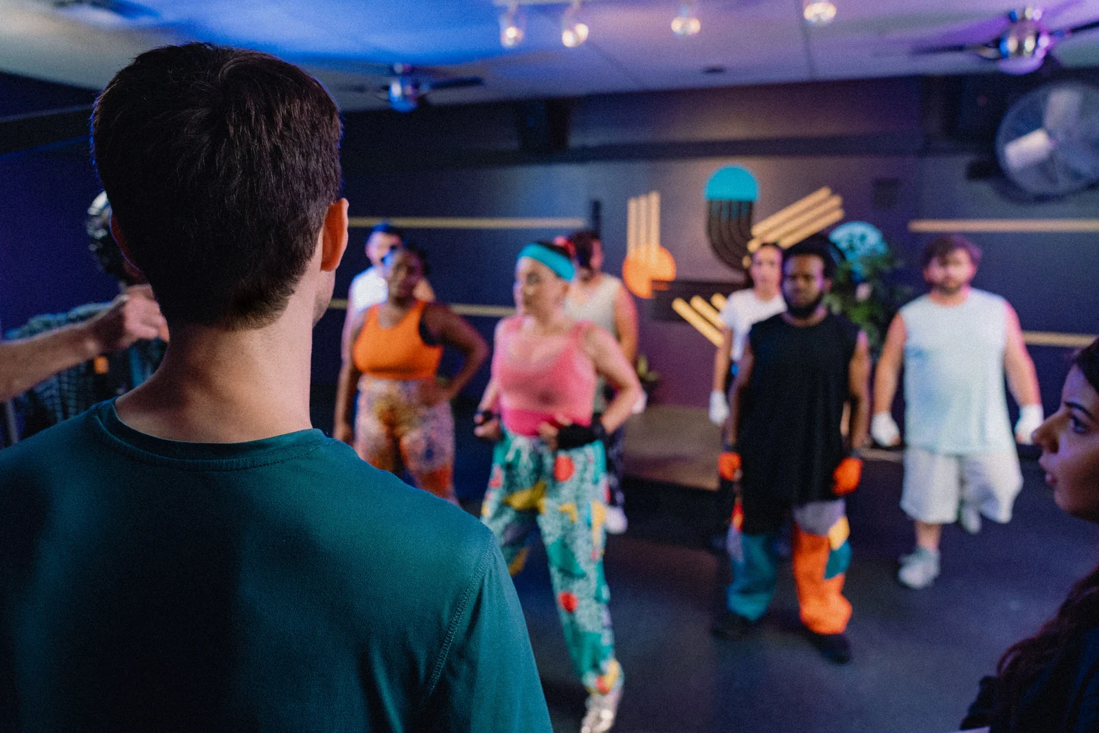 Graham Nolte on a colorful dance-studio set surrounded by performers in vivid costumes