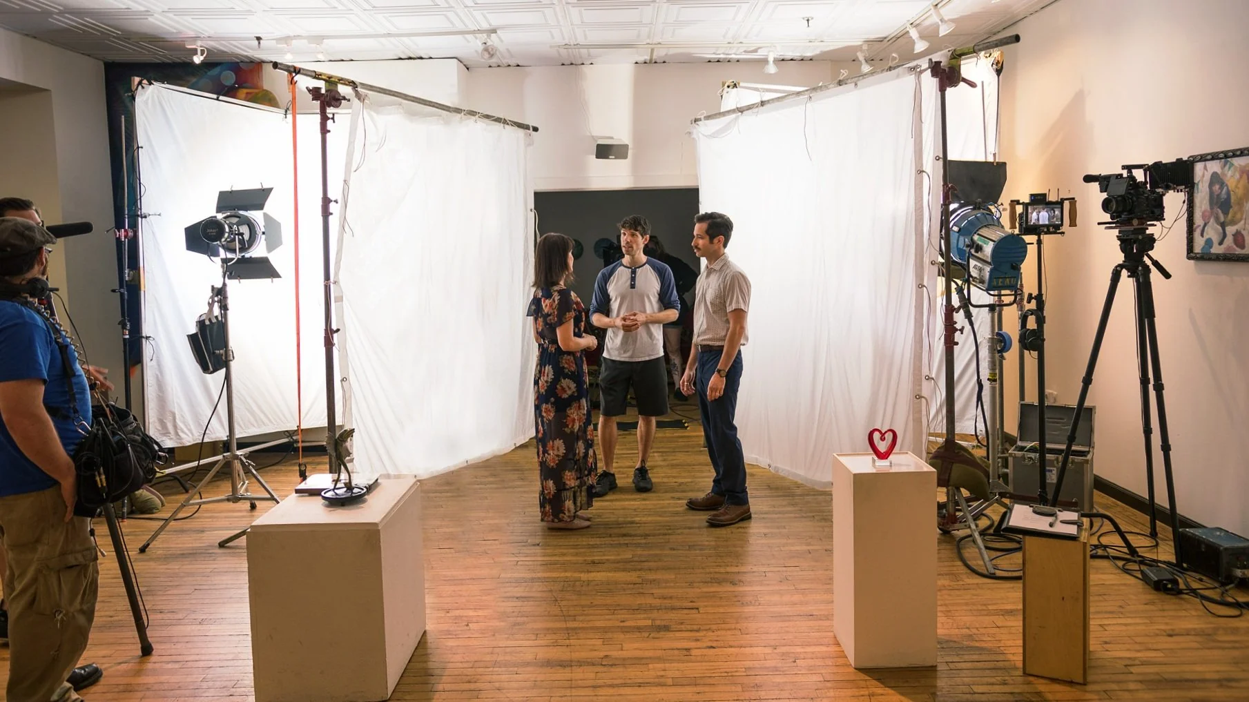 Film set inside a gallery space with lights, a camera on a tripod, and crew talking